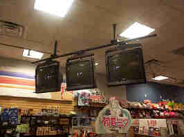 Three CRT televisions hanging from the ceiling of the Fye. Below the TVs is a sign advertising Hatsune Miku merchandise.