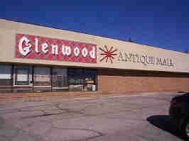 Outside of the Glenwood Antique Mall. The building is brick on the bottom half, and concrete on the top half. "Glenwood" is spelled in an Old English font on a tartan background, and "ANTIQUE MALL" is spelled in serif caps font.