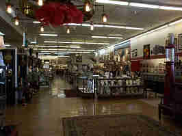 The front of the Glenwood Antique Mall. Cabinets of jewelry line the middle, with rows of shelves to the left, with signs and artworks hanging from the wall on the right.