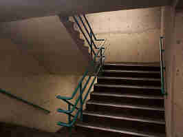 The stairway of the Crown Center parking garage. The stairs are brown carpet with metal trim on the edges, with green handrails in the middle and tan walls to the sides.