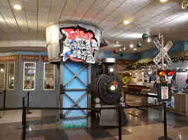 The front of Fritz's in the Crown Center Mall. A model locomotive and "RAILROAD CROSSING" sign sit next to a blue column, supporting the company's logo on a wood barrel.