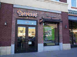 The storefront of the Spencer's in Zona Rosa. The outside is the company's typical brick with concrete base design, with a glass door to the left of a large window advertising store products.