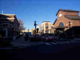 Down another street of the Zona Rosa. To the left and right are various stores, with cars parked on the side of the street. A red Corvette is waiting at the stop sign.