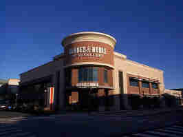 The front of the Zona Rosa Barnes & Noble. The building is made of white and brown concrete, with windows decorating the sides of the building. The entrance is in a cylindrical tower, with the B&N logo proudly at the top.